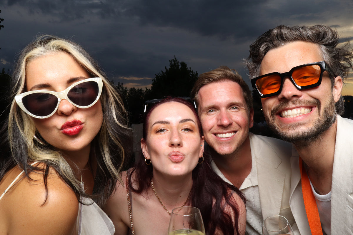 Vier fröhliche Freunde mit Sonnenbrillen machen ein Gruppenfoto mit einer Fotobox auf einem Event in Frankfurt